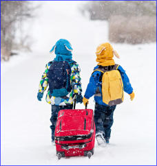 Two young boys pulling suitcase in snow - helping hand